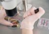 Gloved hands manipulating samples under a microscope in a petri dish