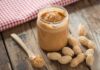 Teen’s Peanut Hack Targets Pesticides Jar of peanut butter with spoon and peanuts on rustic table