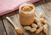 Jar of peanut butter with spoon and peanuts on rustic table