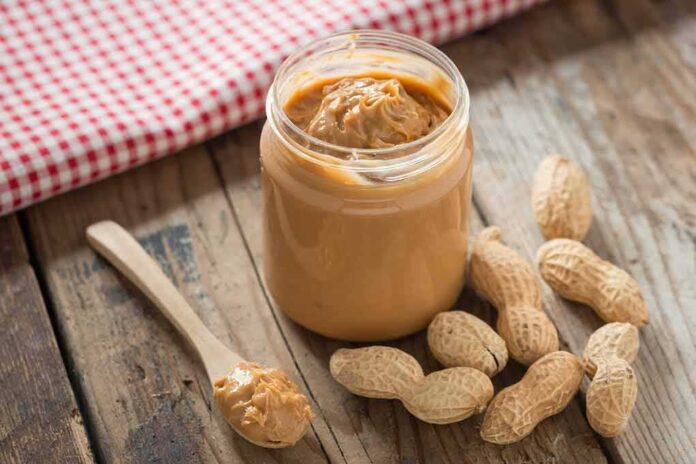 Jar of peanut butter with spoon and peanuts on rustic table