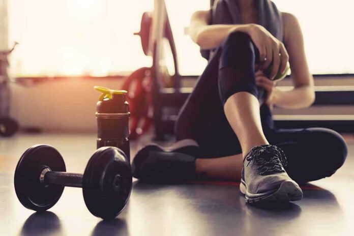 shutterstock_749969473 person resting on gym floor with dumbbell and water bottle