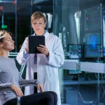 Patient wearing EEG cap sits while clinician reviews data on tablet