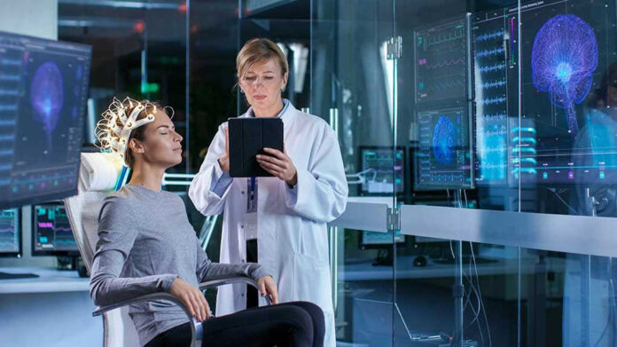 Patient wearing EEG cap sits while clinician reviews data on tablet