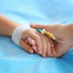 Two hands holding, one with medical IV attached.