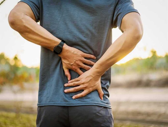 shutterstock_1020731773 Person holding lower back in pain outdoors