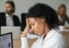 Chronic stress may be quietly reshaping your heart Woman in office holding her head with eyes closed