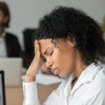Woman in office holding her head with eyes closed