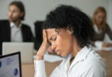 Woman in office holding her head with eyes closed