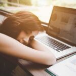 Woman resting her head on desk beside an open laptop