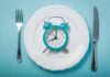 Alarm clock on a white plate with fork and knife