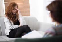 Why The Future Of Wellness Starts Beyond the Individual Woman with hand on forehead sitting on couch during counseling session