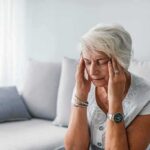 Older woman sitting on a couch holding her temples