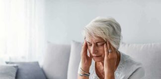 Older woman sitting on a couch holding her temples