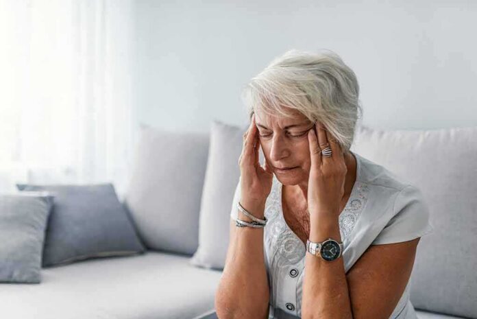 Older woman sitting on a couch holding her temples
