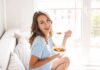 Eat This, Watch Age Markers Tumble Woman sitting on a couch eating a bowl of fruit salad