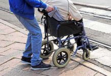 Caregiver pushing person in wheelchair over curb