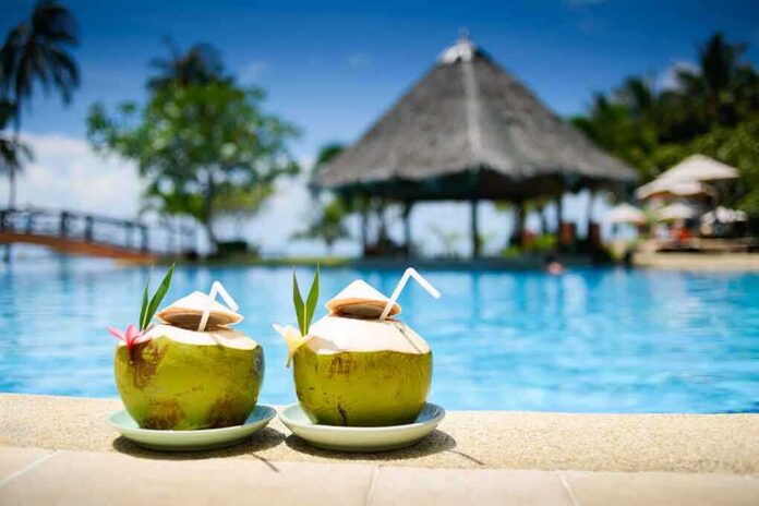 Two coconut drinks with straws beside a swimming pool