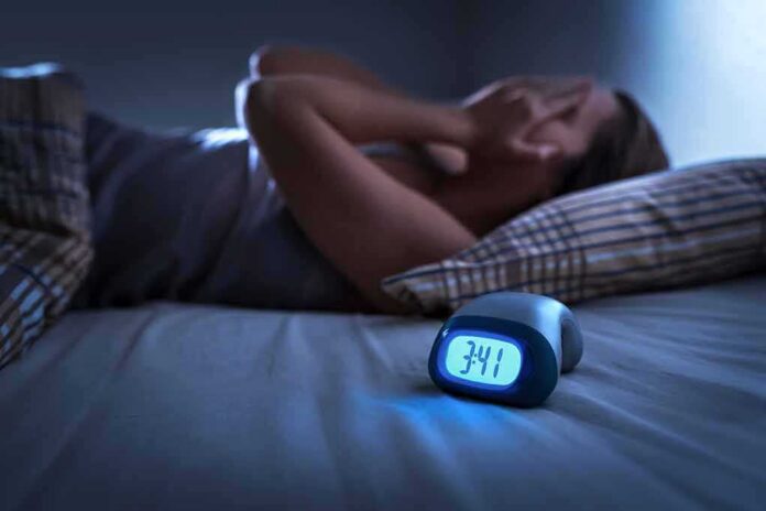 shutterstock_1299304069 Person lying awake in bed beside a glowing digital alarm clock
