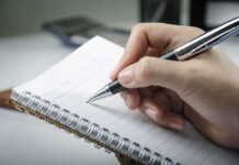 A hand holding a pen above a blank notebook page