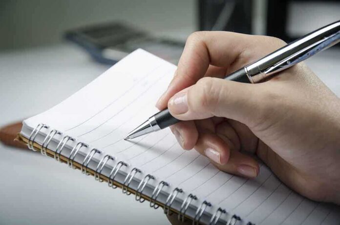 A hand holding a pen above a blank notebook page
