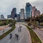 Cyclists on a curved urban road with a modern city skyline