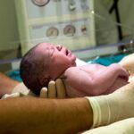 Newborn baby held by gloved medical staff in a hospital