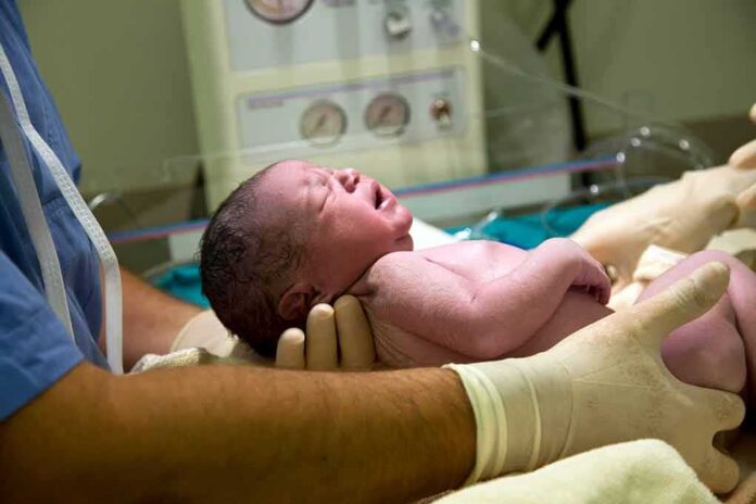 Newborn baby held by gloved medical staff in a hospital