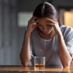 Woman with head in hands at a bar with a glass of whiskey