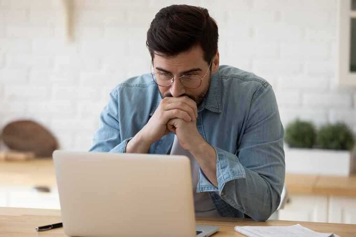 shutterstock_1613076505 Man in glasses looking at laptop with hands clasped near mouth