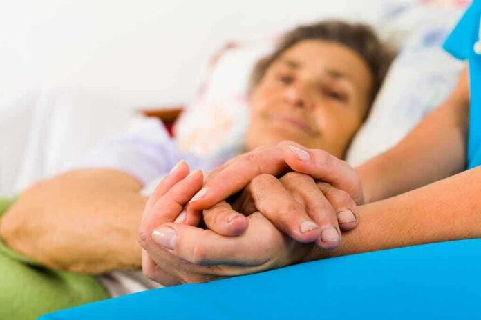 Caregiver holding hands with an elderly patient in bed
