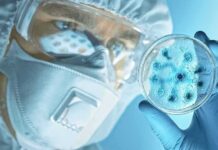 Scientist in protective gear examining a petri dish