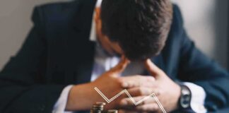 Businessman with head down behind stacks of coins and downward arrow