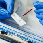 Gloved hands using a rapid test cassette with a blood sample dropper
