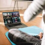 person on yoga mat watching a virtual workout class on a laptop