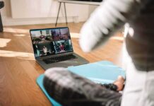 person on yoga mat watching a virtual workout class on a laptop