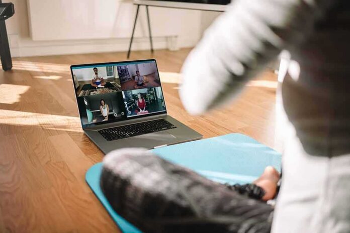 shutterstock_1708844755 person on yoga mat watching a virtual workout class on a laptop