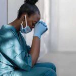 Government Study Flags Vitamin D – Fibroid Tie Healthcare worker in scrubs sitting against a wall with head bowed