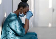 Healthcare worker in scrubs sitting against a wall with head bowed
