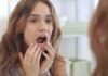 young woman checking inside her mouth in bathroom mirror