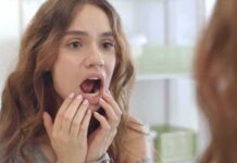young woman checking inside her mouth in bathroom mirror
