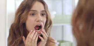young woman checking inside her mouth in bathroom mirror