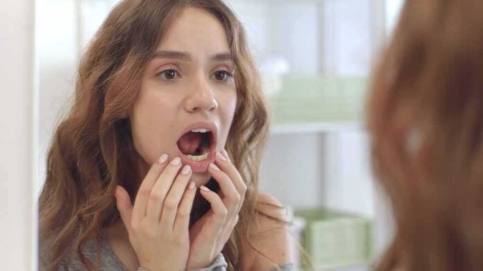 shutterstock_1817315312 young woman checking inside her mouth in bathroom mirror