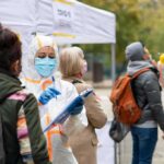 Healthcare workers in PPE assist people at an outdoor COVID-19 testing site