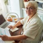 Senior woman with glasses reviewing documents at a kitchen table