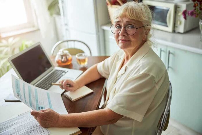 Senior woman with glasses reviewing documents at a kitchen table