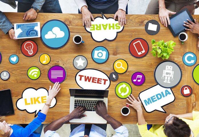 People,Connecting,And,Sharing,Social,Media Top view of a collaborative workspace with social media icons and people using laptops