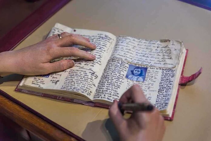 shutterstock_1932112931 Hands writing in an open handwritten diary with a small portrait photo