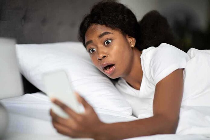 Woman in bed looking shocked at a smartphone