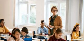 Teacher standing among students in a bright classroom