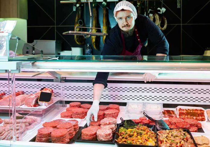 shutterstock_2472086565 Butcher arranging meat patties in display case